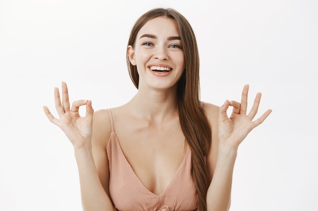 Femme magnifique européenne heureuse optimiste en robe beige à la mode montrant un geste correct ou parfait