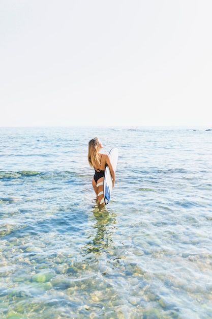 Femme en maillot de bain à pied avec planche de surf en mer bleue