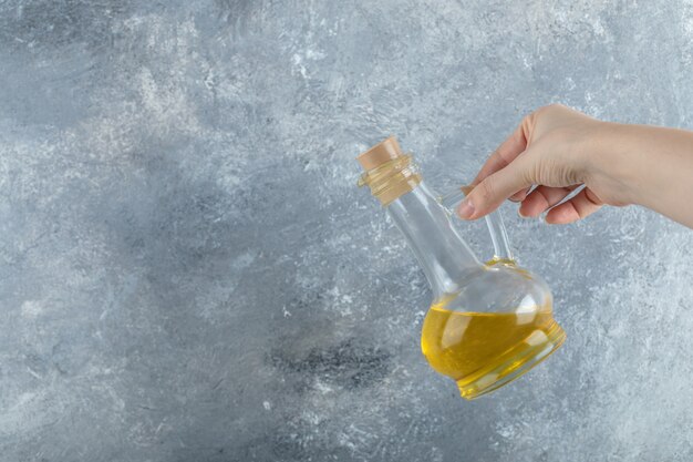 Femme main tenant une bouteille d'huile végétale sur fond gris.