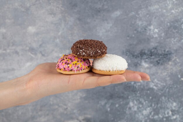 Femme main tenant trois biscuits frais avec des paillettes colorées sur une surface en pierre