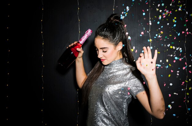 Femme avec les mains en l&#39;air tenant une bouteille de champagne près de lancer des confettis