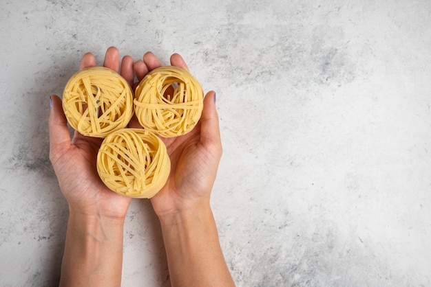 Photo gratuite femme mains tenant des nids de pâtes tagliatelles crues sur fond blanc.