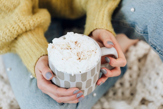 Femme à la maison de boire du chocolat chaud avec de la crème fouettée