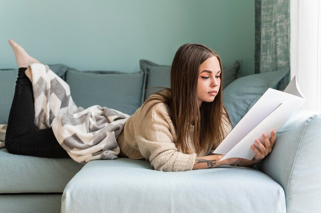 Femme à la maison sur le canapé en lisant un livre pendant la pandémie