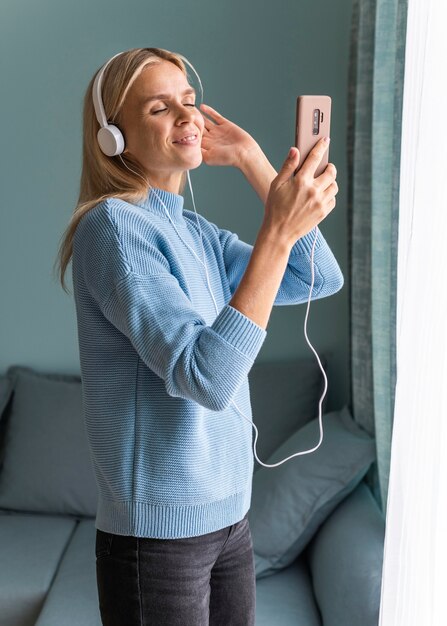 Femme à la maison en écoutant de la musique sur ses écouteurs avec smartphone pendant la pandémie