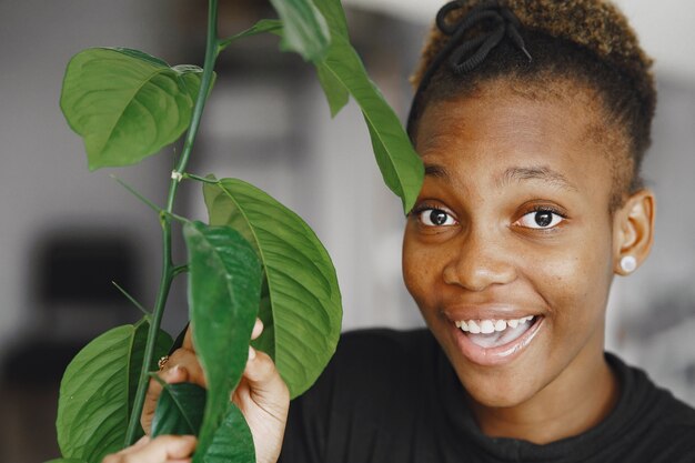 Femme à la maison. Fille dans un pull noir. Femme africaine au bureau. Personne avec pot de fleurs.