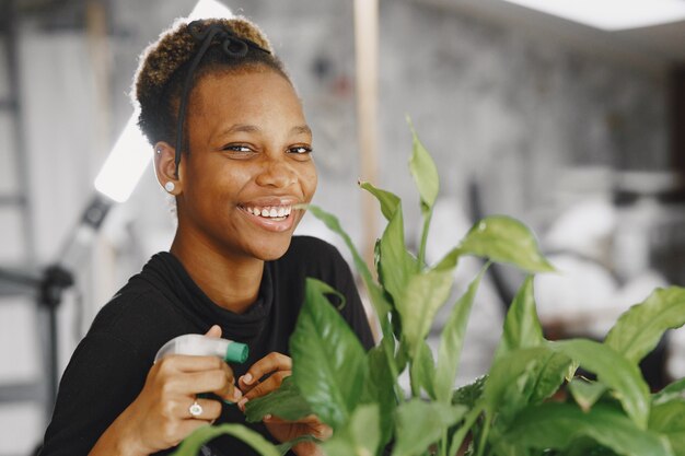 Femme à la maison. Fille dans un pull noir. Femme africaine au bureau. Personne avec pot de fleurs.