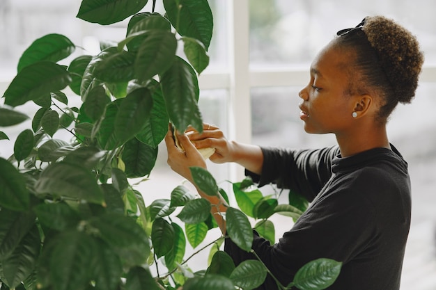 Femme à la maison. Fille dans un pull noir. Femme africaine utilise le chiffon. Personne avec pot de fleurs.