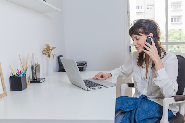 Photo gratuite femme à la maison avec un ordinateur portable parlant au téléphone