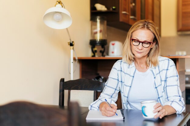 Femme à la maison pendant l'écriture de quarantaine et prendre un café