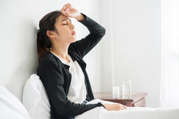 Photo gratuite une femme mal à l'aise est assise sur le lit et a des médicaments sur la table.