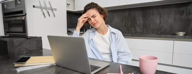 Photo gratuite une femme a mal à la tête alors qu'elle travaille à la maison une fille a une migraine douloureuse s'assoit près de l'ordinateur portable grimaces de