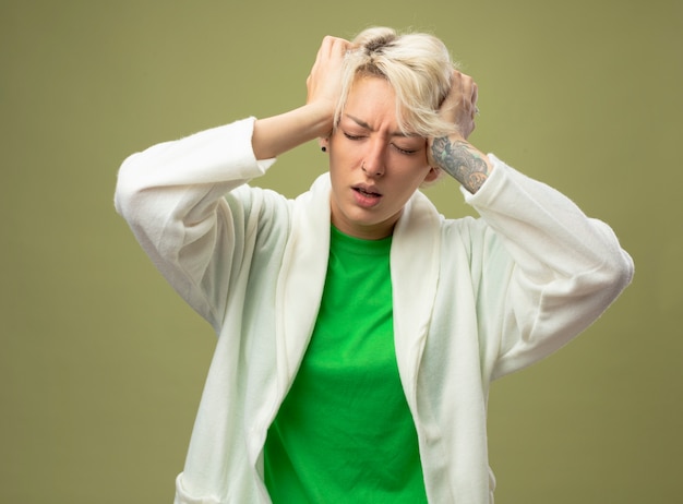 Femme malade aux cheveux courts se sentir mal en touchant sa tête souffrant de forts maux de tête debout sur fond clair