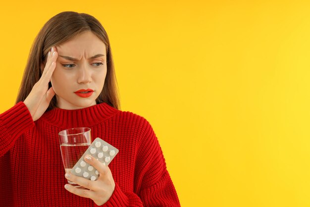 Femme malade avec des pilules et de l'eau sur fond jaune