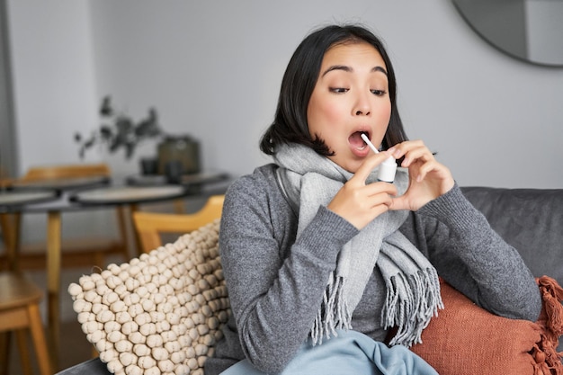 Photo gratuite femme malade utilisant un spray de mal de gorge traitant son rhume ou sa grippe restant à la maison en congé de maladie assis