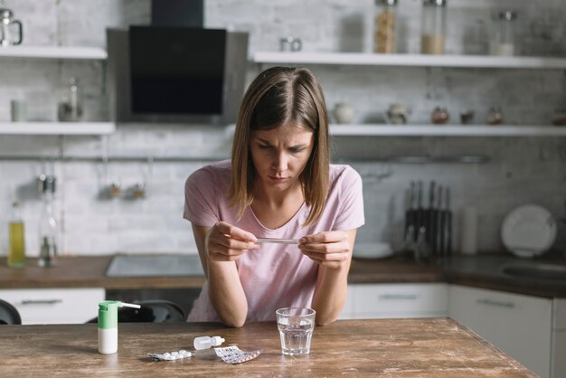 Femme malade, vérifier la température sur le thermomètre avec des médicaments sur le bureau en bois