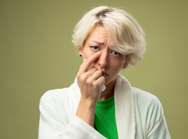 Femme malsaine malade avec les cheveux courts se sentir mal en pointant avec le doigt sur son nez d'être malheureux debout sur un mur léger