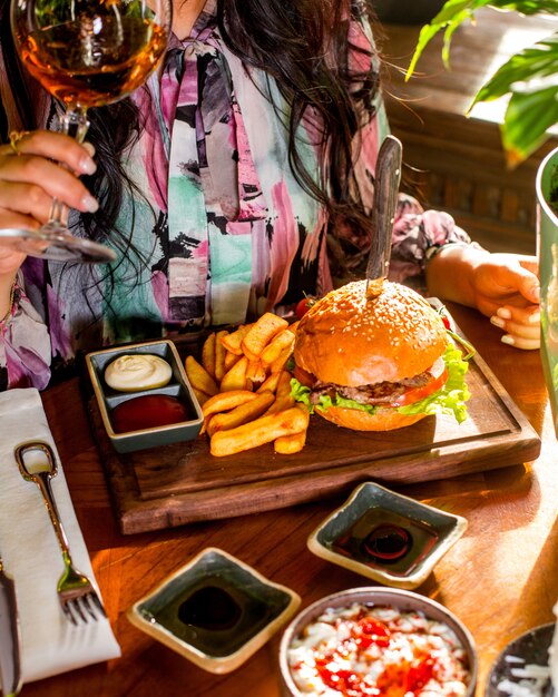 Femme mange un burger servi avec des frites, du ketchup et de la mayonnaise