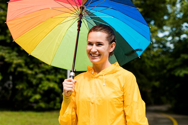 Femme en manteau de pluie souriant tout en tenant un parapluie