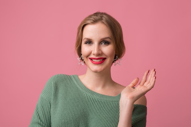 femme avec maquillage élégant, lèvres rouges, pull vert posant sur rose