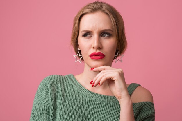 femme avec maquillage élégant, lèvres rouges, pull vert posant sur rose