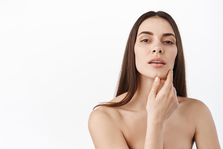 Photo gratuit femme avec maquillage naturel et portrait de peau saine. beau modèle féminin touchant la peau du visage hydratée et éclatante sur un mur blanc en gros plan. concept de soins de la peau