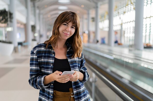 Femme marchant dans l'aéroport à l'aide de son smartphone.