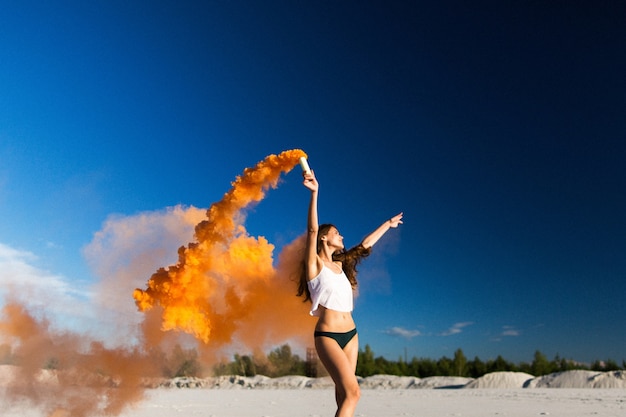 Femme marche avec de la fumée d&#39;orange sur la plage blanche sous le ciel bleu