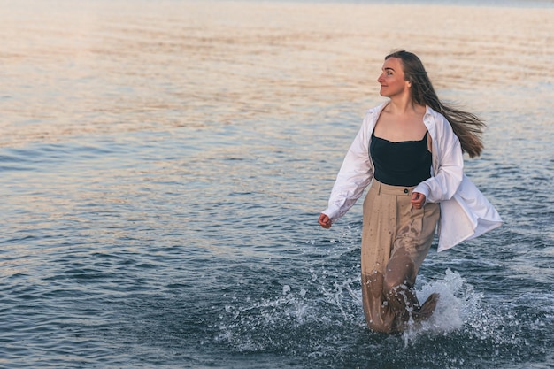 Une femme marche le long de la mer pieds nus au coucher du soleil copie espace