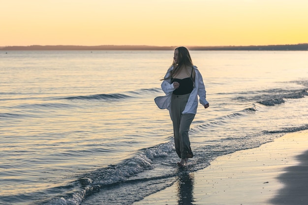 Une femme marche le long de la mer pieds nus au coucher du soleil copie espace