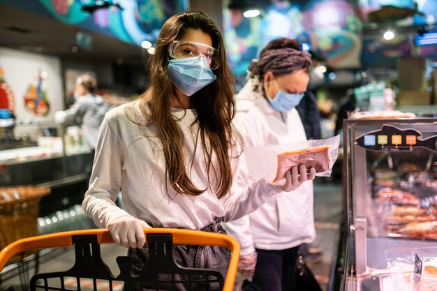 Femme avec le masque chirurgical et les gants fait ses courses au supermarché