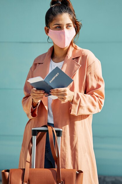 Femme avec masque médical à l'aéroport et passeport pendant la pandémie