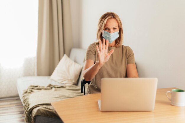 Femme avec masque médical et appel vidéo d'ordinateur portable pendant la quarantaine