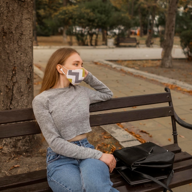 Femme avec masque médical assis sur un banc