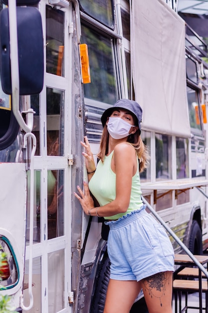 Femme en masque médical blanc à pied autour de la ville se dresse en bus café sur la place de la ville
