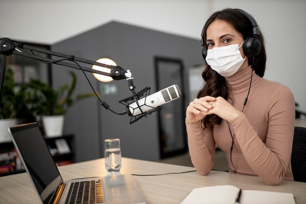 Femme avec masque médical diffusant à la radio avec microphone