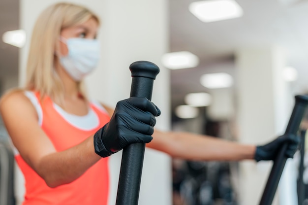 Femme avec masque médical et gants travaillant à la salle de sport