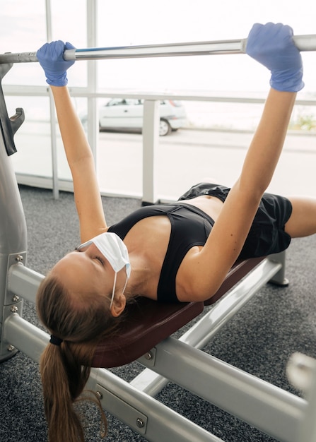 Femme avec masque médical et gants travaillant à la salle de sport