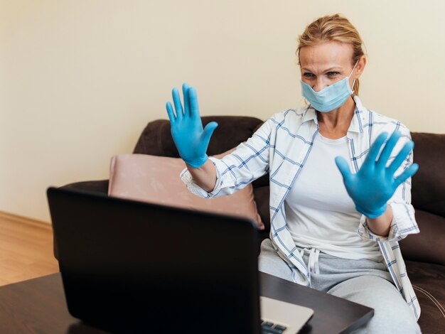 Femme avec masque médical à la maison pendant la quarantaine travaillant sur ordinateur portable