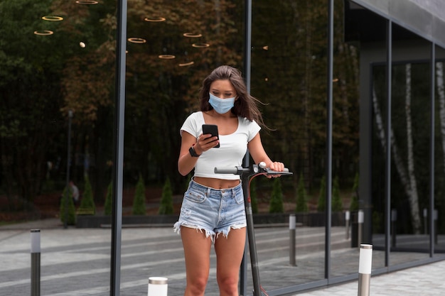 Femme avec masque médical et scooter à l'extérieur