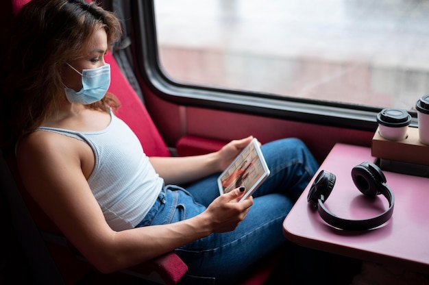 Femme avec masque médical utilisant une tablette lors d'un voyage en train public