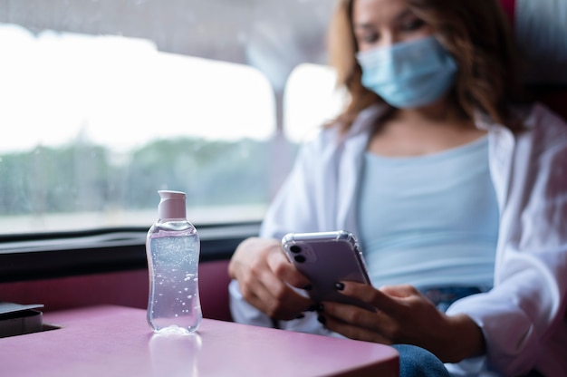 Femme avec masque médical voyageant en train public et utilisant un smartphone