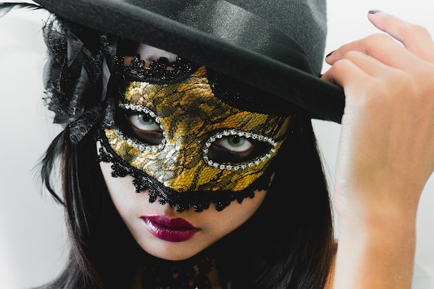 Femme avec un masque vénitien d&#39;or et un chapeau noir sur un fond blanc