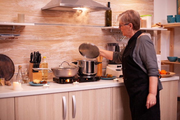 Femme Matue vérifiant la nourriture pendant la cuisson pour le dîner avec son mari senior. Femme à la retraite cuisinant des aliments nutritifs pour elle et son homme pour célébrer l'anniversaire de la relation.