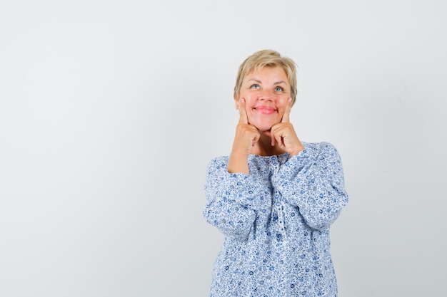 Femme mature en chemise en gardant les doigts sur les joues et à la jolie