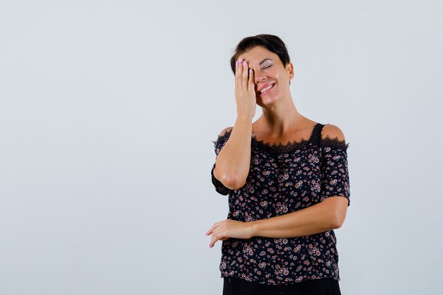 Femme mature en chemisier couvrant les yeux avec la main et à la vue de face, heureux.