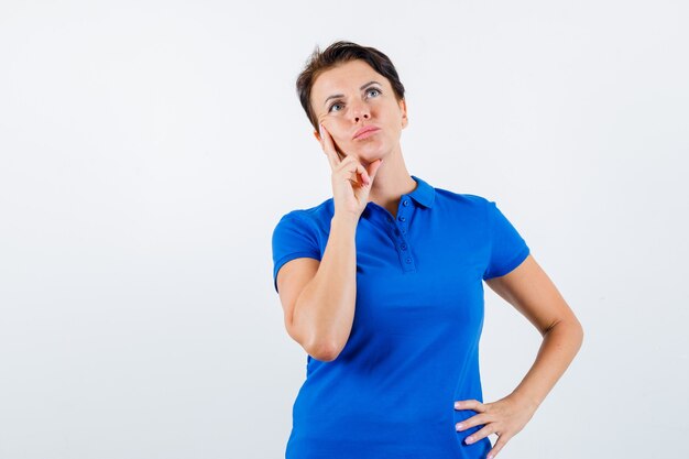 Femme mature debout dans la pensée pose en t-shirt bleu et à la vue douteuse, de face