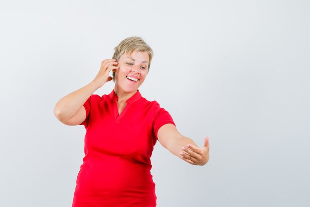 Femme mature faisant semblant de passer un appel vidéo en t-shirt rouge et à la fringante.