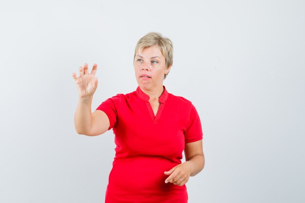 Femme mature faisant semblant de tenir quelque chose de minuscule en t-shirt rouge et à la recherche concentrée.