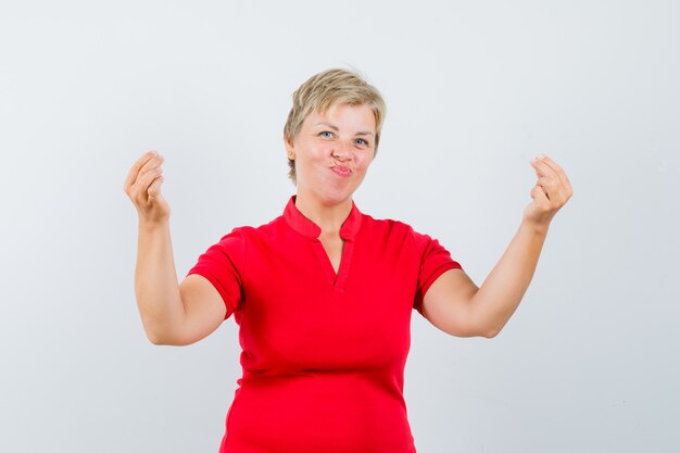 Femme mature montrant le geste de l'argent en t-shirt rouge et à la joyeuse.